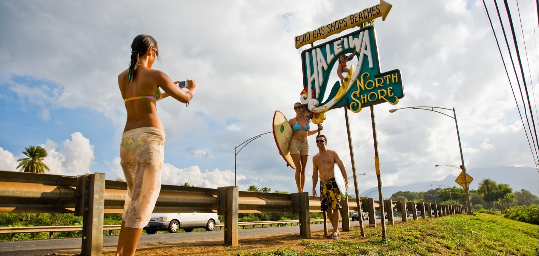 Woman taking a picture of a couple next to the Haleiwa sign