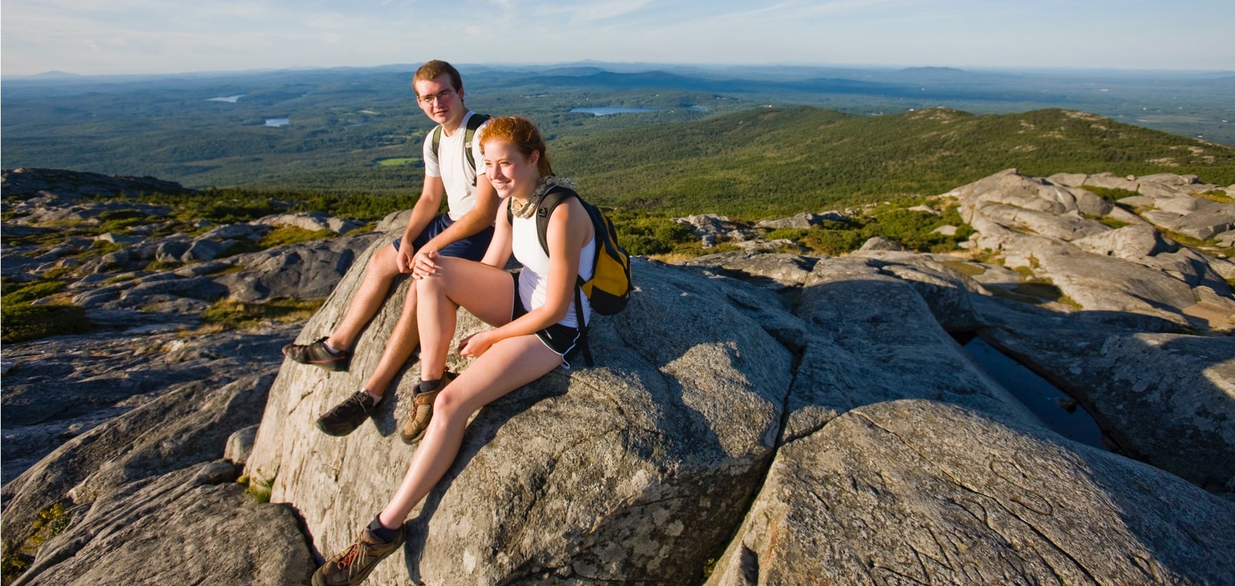 A young couple takes a break from hiking on the summit of Mount Monadnock in New Hampshire's Monadnock State Park.